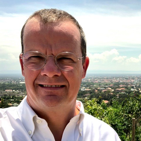 Portrait of Alexander Crawford with buildings, trees and a cloudy sky in the background.