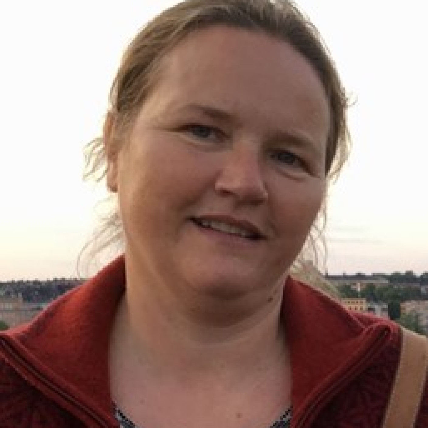 Portrait of Maria Johansson with a cloudy sky and buildings in the background.